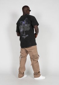 Sort grafik t-shirt med sommerfuglemotiv på ryggen, parret med beige cargo bukser med sidelommer, båret med hvide sneakers.