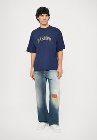Marineblå t-skjorte med korte ermer med «BARROW» i gullbokstaver, parret med falmede blå vide jeans med lapper og hvite sneakers.