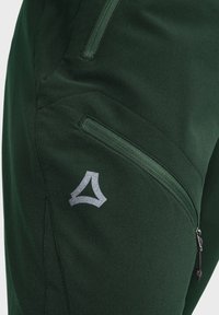 Dark green pants made of a textured fabric, featuring a zippered side pocket and a silver logo accent on the lower leg.