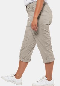 Béžové capri kalhoty vyrobené z lehkého materiálu, s ohrnutými lemy, bočními kapsami a viditelnými švy. V páru s bílými teniskami.