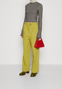 Maglietta a maniche lunghe a righe bianche e nere, pantaloni gialli a vita alta, stivali platform verdi in vernice e una borsa geometrica rossa.