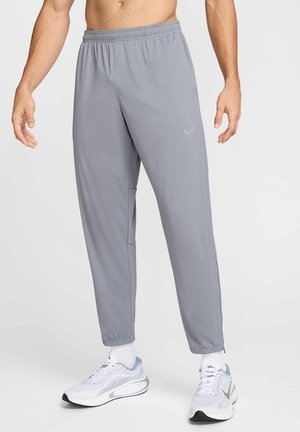Pantalons de sport gris avec une taille élastique, dotés de poches latérales zippées et d'un petit logo Nike sur la cuisse gauche.
