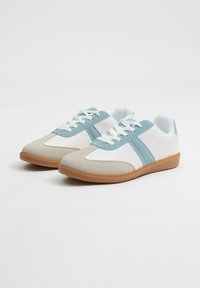 Zapatillas deportivas blancas y azul claro con una textura suave, que presentan dos franjas azules, una puntera redondeada y una suela de goma.