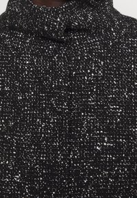 Svart tyg med en texturerad mönstring som har vita fläckar. Materialet är vävt och ger en subtil djup och intresse i utseendet.