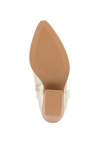 Zapato de tacón beige con puntera afilada y suela texturizada. Presenta una suela de goma marrón y un pequeño tacón cuadrado.
