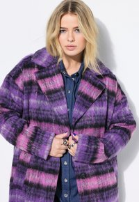 Paarse en roze gestreepte jas met een brede kraag en grote knopen. Zachte textuur, oversized pasvorm, gelaagd over een blauwe denim shirt.