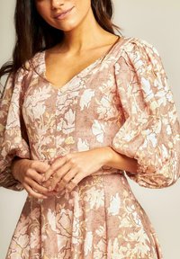 Bloemmotief jurk in zachte roze en beige tinten. Kenmerkt zich door poffende mouwen, een V-halslijn en een getailleerde taille. Soepele textuur.