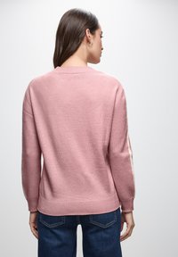 Rosa gestrickter Pullover mit rundem Ausschnitt und gerippten Bündchen, ausgestattet mit weißen Seitenstreifen. Weiche Textur und entspannter Schnitt.