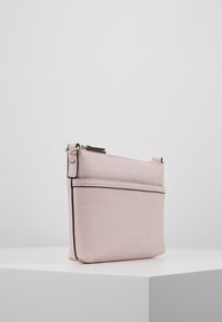 Kompakti vaaleanpunainen nahkainen olkalaukku, jossa on vetoketjusuljenta, etutasku ja hopeanväriset yksityiskohdat. Sileäpintainen rakenne ja minimalistinen muotoilu.