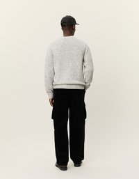 Pull en maille gris clair avec une finition texturée, associé à un pantalon cargo en velours côtelé noir avec poches latérales et coupe décontractée. Casquette noire à motif à carreaux.