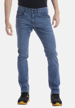 Un jean en denim bleu clair avec une coupe ajustée, cinq poches, une fermeture éclair avec un bouton, et un léger décoloration sur l'ensemble du tissu.