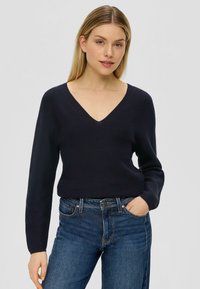 Marineblauer V-Ausschnitt-Pullover mit langen Ärmeln, aus einem strukturierten Strickstoff, kombiniert mit eng anliegenden blauen Jeans.