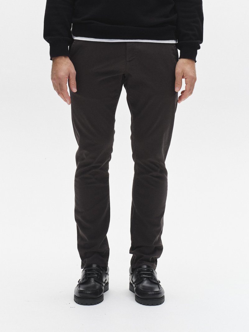 Dunkelbraune, schlanke Hose aus leichtem Stoff mit glatter Textur und Seitentaschen, kombiniert mit schwarzen Schnürschuhen.