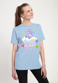 Světle modré tričko s kresleným medvědem na oblacích, s textem "CARE BEARS FOREVER" v tučných, barevných písmenkách a hvězdami.