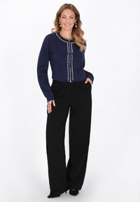 Sudadera corta azul marino con detalles decorativos de botones y mangas largas, combinada con pantalones negros de pierna ancha y cintura alta.