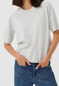 Pull gris clair à manches courtes en maille douce avec un col rond. Associé à un jean en denim bleu avec des poches arrière.