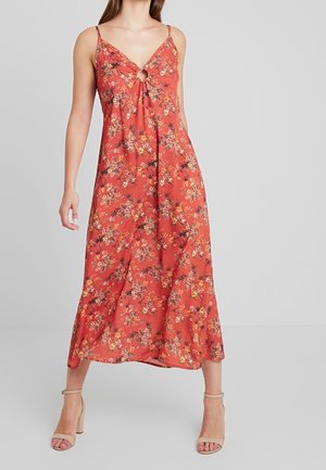 Robe maxi florale rouge avec un décolleté en V et un détail en trou de serrure. Le tissu est lisse et léger, avec un mélange de fleurs orange, jaunes et vertes.