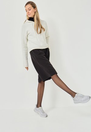 Haut à capuche gris clair texturé avec cordons, shorts noirs, collants noirs transparents et baskets gris clair, le tout sur un fond blanc.