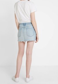 Gonna mini in denim azzurro chiaro con orlo sfrangiato, design a cinque tasche e vita alta, abbinata a una t-shirt bianca e scarpe da ginnastica bianche.