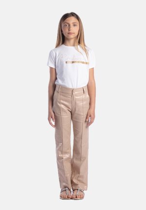 Maglietta bianca con testo glitterato "Couture", abbinata a pantaloni high-waisted beige lucidi e sandali piatti con cinturini decorativi.