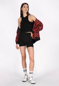 Top crop senza maniche nero, pantaloni corti neri a vita alta, giacca bomber con stampa leopardata rossa e nera, calze bianche con strisce nere, sneakers bianche.