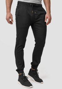 Pantalones de chándal negros en un diseño ajustado con puños elásticos, cintura con cordón y bolsillos laterales, fabricados con una tela suave y ligera.