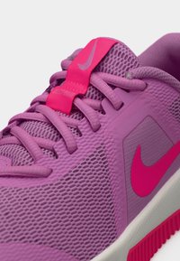Αθλητικό παπούτσι Nike με πλέγμα στο επάνω μέρος σε αποχρώσεις του μωβ και ροζ, με υφή σχεδίασης και έντονο λογότυπο στη γλώσσα και στην πλευρά.