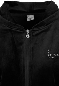 Crna baršunasta hoodie na zatvarač s povlačenjem u obliku srca i logom u bijeloj vezbi na prednjoj strani.