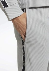 Grå ribbade träningsbyxor med en sidficka och ett svart mönstrat rand längs den yttre sömmen. Texturerad tyg förbättrar grepp och komfort.