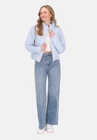 Giacca imbottita blu chiaro con colletto alto, zip frontale e dettagli rosa, abbinata a jeans blu a vita alta e scarpe da ginnastica bianche.