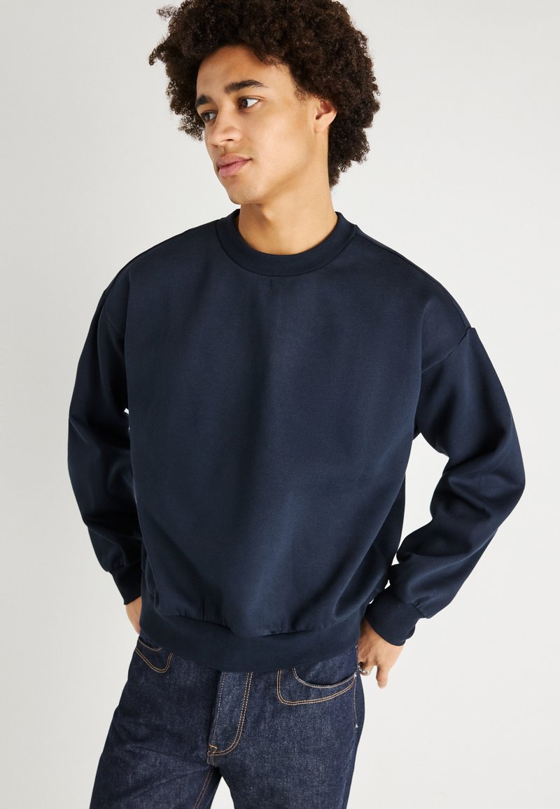 Navy blue sweatshirt made of cotton blend fabric, featuring a crew neckline, long sleeves, and a relaxed fit with ribbed cuffs and hem.