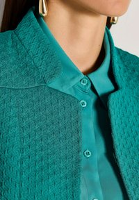 Teal textuuroverhemd met een gladde kraag, voorzien van twee knopen en complexe patronen op de stof voor visuele aantrekkingskracht.