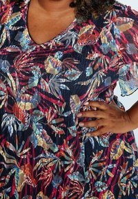 Haut à imprimé floral avec un fond bleu marine, motifs de feuilles multicolores, col en V et manches courtes fluides. Tissu texturé.