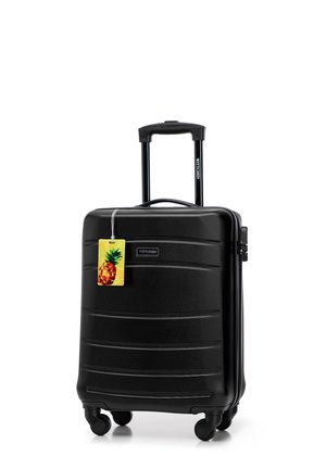 Black hardshell suitcase with a textured surface, retractable handle, four wheels, and a pineapple-themed luggage tag attached.