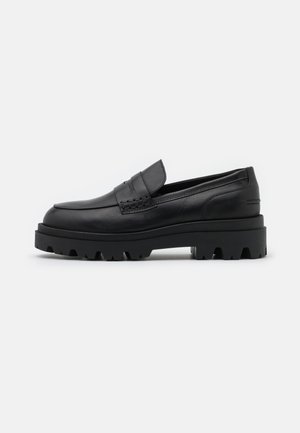 Mocassins en cuir noir avec une semelle en caoutchouc épaisse, dotés d'un détail tressé sur le devant et d'une silhouette épurée.