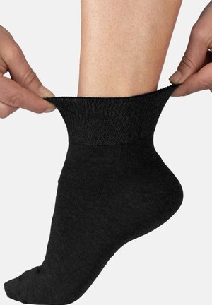 Black sock being pulled over a foot; ribbed cuff, smooth texture, fitted design, and no visible patterns or accents.