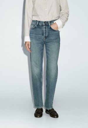 Jeans in denim blu chiaro a gamba dritta con un classico design a cinque tasche. Indossati con una camicia a maniche lunghe a righe bianche e blu e mocassini.
