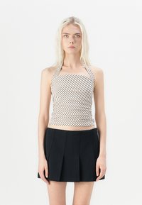 Halter-neck top in cream with brown diagonal stripes, featuring ruched detailing. Paired with a black pleated mini skirt.