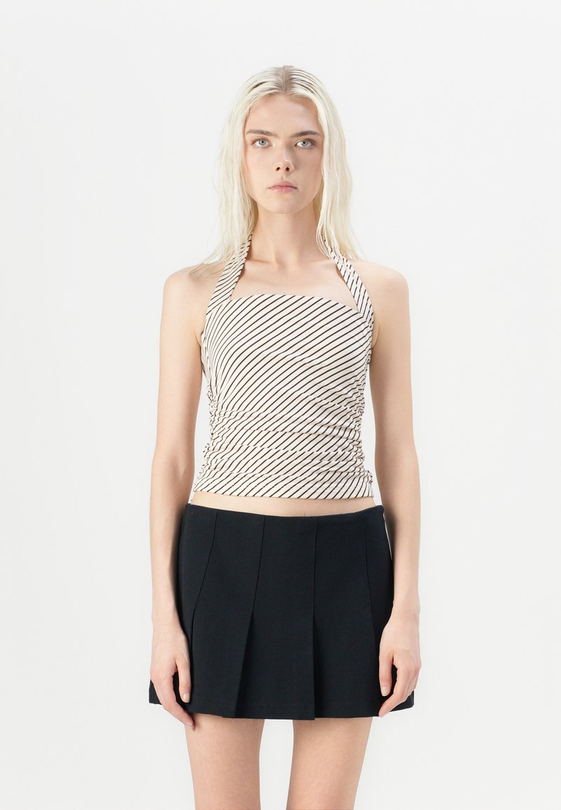 Top de cuello halter en crema con rayas diagonales marrones, con detalles fruncidos. Combinado con una falda corta plisada negra.