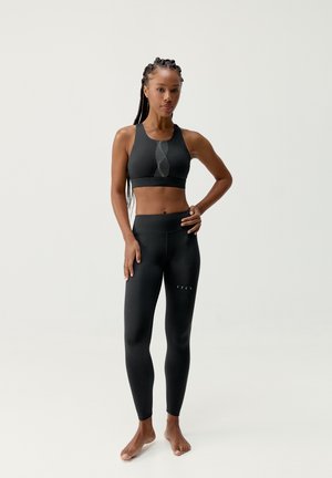 Black sports bra with a decorative mesh pattern at the center, paired with high-waisted black leggings featuring subtle branding on the leg.