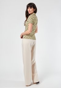 Maglione polo in verde pallido con un motivo geometrico; abbinato a pantaloni beige chiaro a gamba larga. Il tessuto appare liscio e leggero.