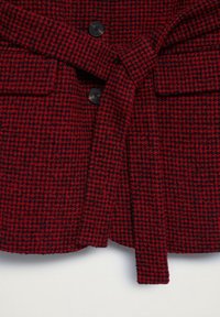 Czerwona i czarna kurtka w kratę z paskiem, dwoma przednimi kieszeniami i czarnymi guzikami. Teksturowany materiał o wyraźnym kształcie.