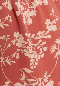 Tissu avec un fond rose poussiéreux et de légers motifs floraux beige mettant en avant des feuilles et des bouquets de fleurs, présenté avec des plis doux.