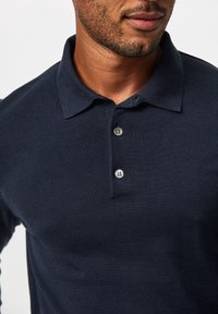 Marineblaues Poloshirt aus weichem Stoff mit schmalem Kragen, dreiknöpfiger Knopfleiste und strukturierter Strickware, die Nahaufnahmen der Details am Halsbereich zeigt.