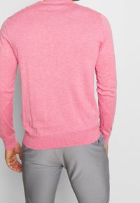 Maglione rosa lavorato a maglia con collo rotondo, maniche lunghe e orlo a coste. Texture morbida, vestibilità casual, senza motivi visibili o dettagli in metallo.