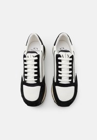 Baskets noir et blanc présentant un mélange de matériaux en textile lisse et en daim, avec une tige en mesh texturé et des lacets contrastants.