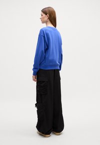 Felpa blu dal taglio rilassato con polsini a costine, abbinata a pantaloni cargo neri oversize con molteplici tasche e dettagli arricciati.