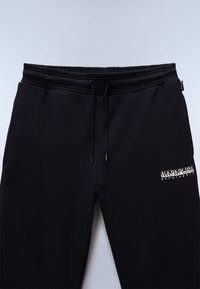 Czarne spodnie dresowe wykonane z miękkiego materiału, z elastycznym paskiem w talii ze sznurkami oraz małym logo na prawej udzie.
