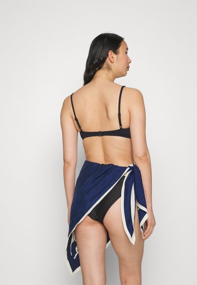 Saia envolvente azul-marinho com uma bainha branca, atada na cintura, combinada com um fundo de biquíni preto. Tecido suave com uma aparência texturizada.