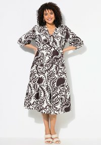 Mustavalkoinen painettu mekko V-päällä, kolmannes hihasta ja kerroksellinen hame. Teksturoidussa kuosissa on pyörivää muotoilua.